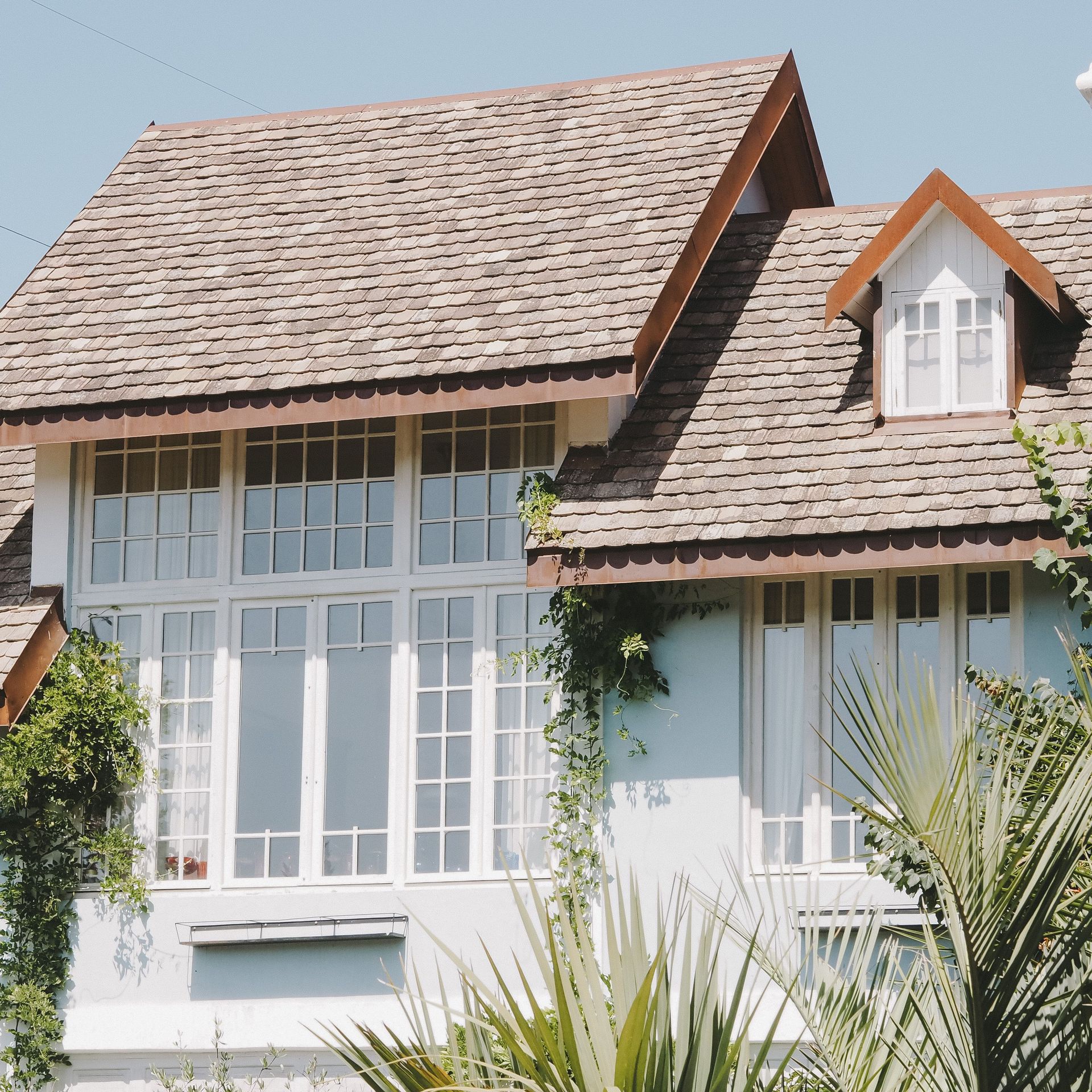 Elegant suburban house with large windows and a shingled slate roof in sunlight.